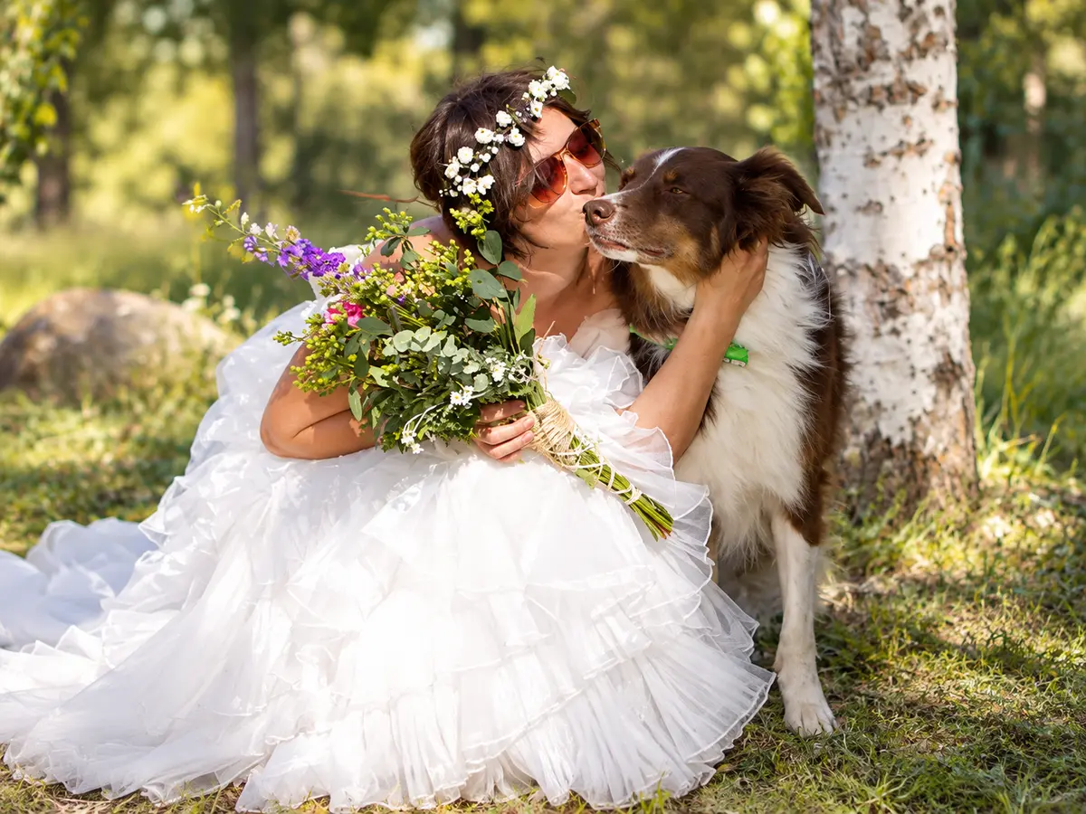 A bride in a flower crown kissing her dog on the cheek